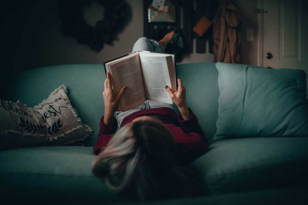 nainen lukee kirjaa rennosti sohvalla maaten