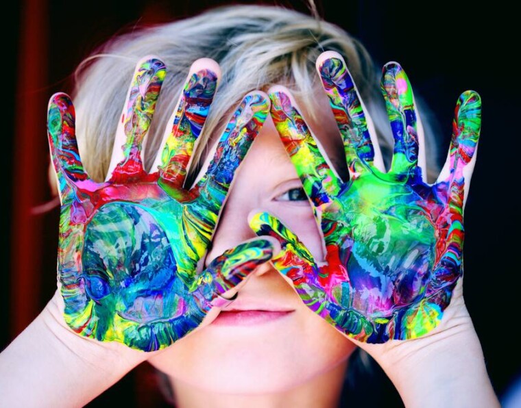 Lapsi näyttää maalista värikkäitä käsiään